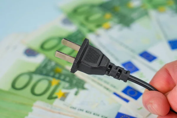 Power plug in hand on euro money background. Expensive electricity supply concept