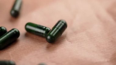 Yeşil doğal destek kapsülleri yavaş çekimde kağıt yüzeyine düşüyor.