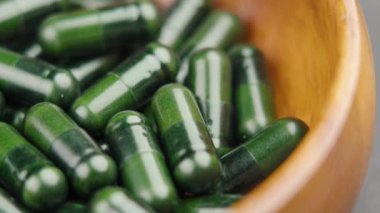 Dolu ahşap bir kase yeşil doğal destek kapsülü. Döndürme