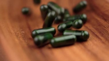 Vitamin takviyesi yeşil haplar kasenin ahşap yüzeyine yavaş çekimde düşüyor.