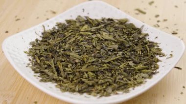 Sencha yeşil çay, beyaz bir fincan altlığında kuru yapraklar. Döndürme