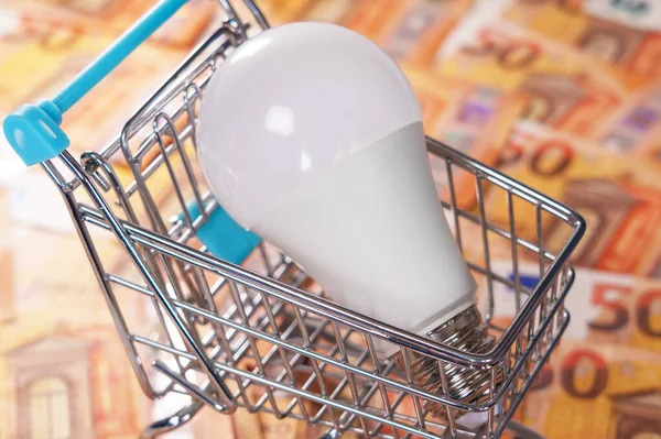 Electric energy saving bulb in a mini shopping cart on a money euro background. Electrical costs concept