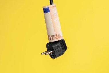 Siyah fişi olan bir elektrik kablosunun üzerine Euro banknotu. Yaratıcı sarı arka plan. Kavramsal görüş. Yüksek enerji maliyeti kavramı.