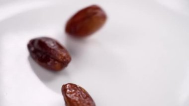 Olgun tropik hurma meyveleri yavaş çekimde beyaz bir seramik tabağa düşüyor. Sağlıklı besleyici yiyecekler