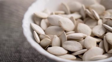 Beyaz kavrulmuş kabak çekirdekleri seramik bir kaseye düşüyor. Besleyici besin bileşeni