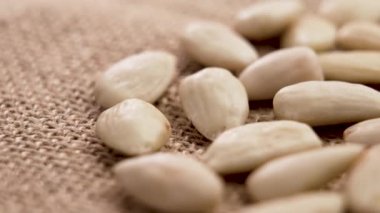 Çiğ çuval bezi üzerinde organik kabuklu badem taneleri. Soyulmuş çiğ fındık. Kapat.
