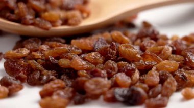 Dağıtılmış koyu kahverengi kuru üzüm meyveleri ve ahşap kaşık. Kurumuş olgun üzümler. Sağlıklı malzeme. Döndürme