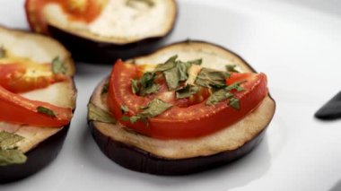 Beyaz seramik tabakta domatesli patlıcan dilimi ve kişniş servis ediliyor.