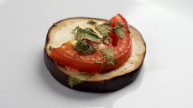 Kızarmış domatesli ızgara patlıcan dilimi ve beyaz seramik tabakta kişniş. Döndürme