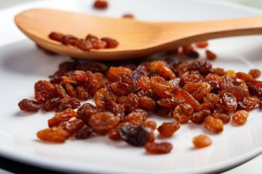 Dağıtılmış koyu kahverengi kuru üzüm meyveleri ve ahşap kaşık. Kurumuş olgun üzümler. Sağlıklı bileşen