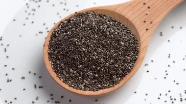 Beyaz seramik çanak üzerinde tahta kaşıkta sağlıklı çiğ chia tohumları. Döndürme