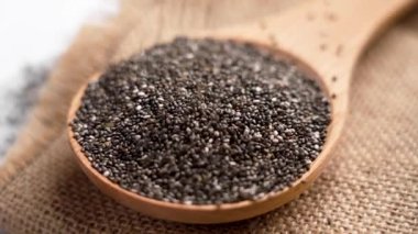 Sağlıklı organik chia tohumları mutfağın ahşap bir kaşığının üzerine dökülüyor. Döndürme