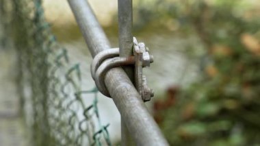 Asma köprünün tırabzanı için başlıklı kıskaç tamir ediliyor. Nehrin üzerinde tel örgüler var. Yakın plan.