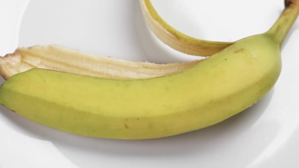 手は白い陶磁器の版の閉鎖からの黄色いバナナの皮を取ります — ストック動画
