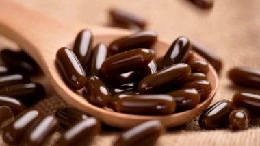 Lecithin kahverengi softgel kapsülleri ağır çekimde sert çuval bezi ile tahta bir kaşığa düşüyor. Beslenme takviyesi