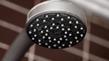 Kahverengi banyo duvarındaki paslanmış kireçlenmiş duş başlığından akan su.