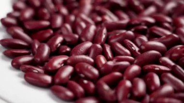 Beyaz seramik bir yüzey üzerinde kırmızı fasulye ağır çekimde hareket eder.