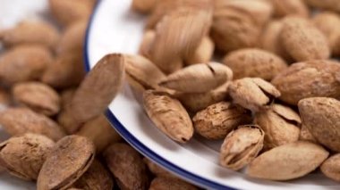 Kırık kabuklu kavrulmuş bademler seramik tabağa düşüyor. Tatil sağlıklı ikramlar. Döndürme. Yavaş çekim