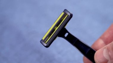 Tek kullanımlık mavi jilet, elinde keskin bıçaklar, kot pantolon arka planında. Hijyen aksesuarları. Kapat.