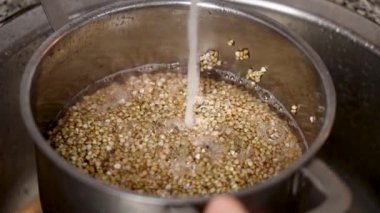 Mutfaktaki tencerede akan suyla karabuğday taneleri pişirme işlemi yavaş çekimde lavaboyu kapatır.