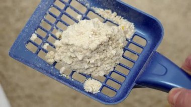 Plastik bir kepçeyle tepsinin üzerine yığılmış kedi idrarı ve doğal çöp.