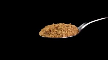 Siyah arka plan üzerine dökülen kaşık dolusu kahverengi kamış şekeri. Doğal besleyici tatlandırıcı
