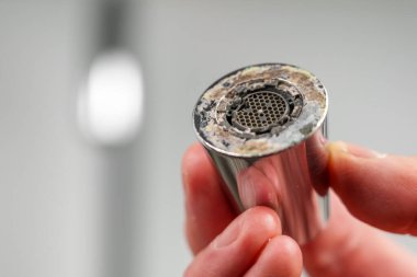 Bir muslukçu mutfak odasında limon skalası olan bir krom musluk havalandırıcısı tutuyor. 
