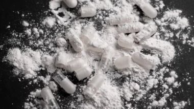Siyah bir masanın üzerine yığınla beyaz toz ve açık tıbbi kapsüller. Uyuşturucu partisi ve uyuşturucu bağımlılığı konsepti. Döndürme. Üst görünüm