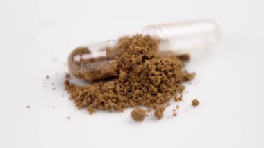 Bitkisel ilaç tozu ve beyaz arka planda açık tıbbi kapsül yakın plan. Döndürme