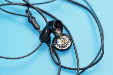 Kırık siyah kulaklık ve mavi bir arka plan. Makro çekim