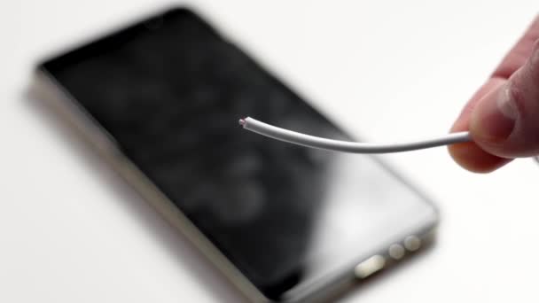 Tangan Memegang Kabel Charger Rusak Dengan Smartphone Hitam Pada Latar — Stok Video