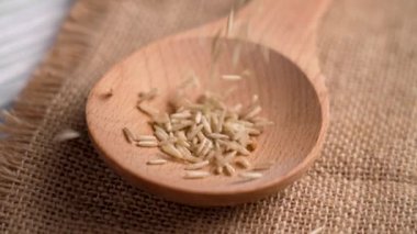 Çiğ, cilalanmamış basmati pilavı kahverengi bir tahta kaşığa kaba kumaş üzerinde düşüyor. Sağlıklı organik malzemeler. Döndürme