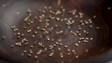 Organik bembeyaz susam tohumları kırsal bir kaseye düşüyor. Geleneksel Hint baharatı. Kapatın. Döndürme. Yavaş çekim