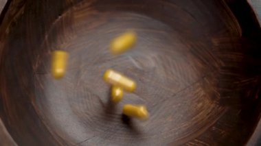 Safra kesesi (curcuma) destek kapsülleri yavaş çekimde ahşap bir kaseye düşüyor. Curkimin tozlu sarı bitkisel ilaç hapları. Döndürme