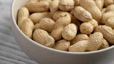 Kabuklu kavrulmuş fıstık dolu seramik bir kase. Bütün kabuksuz yer fıstıkları kapanıyor. Döndürme
