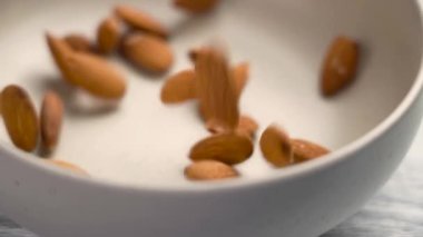 Çiğ badem fıstığı mutfak seramik kasesine düşüyor. Sağlıklı taze malzemeler. Döndürme. Yavaş çekim