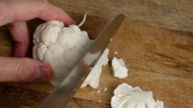 Tahta bir mutfak doğrama tahtasının üzerinde bıçakla karnabahar doğramak. Sebze malzemeleri hazırlanıyor.