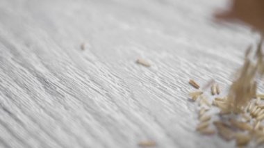Rafine edilmemiş basmati pirinç tohumları bir pazar paketinden kırsal bir tahta üzerinde yavaş çekimde düşüyor.
