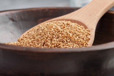 Kahverengi kasede ahşap kaşıkla susam tohumları. Mutfak malzemeleri kapanıyor.