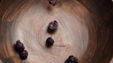 Kurumuş kırmızı kirazlar ağır çekimde ahşap bir kaseye düşüyor. Sağlıklı vitamin malzemeleri kapanıyor. Döndürme