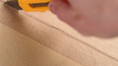 Alınan karton kutuyu açan kişi, kağıt yapıştırıcısını keskin bir kesici bıçakla kesiyor.