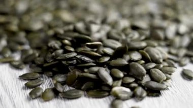 Organik kabak çekirdekleri beyaz tahta dokusuna yavaş çekimde düşüyor. Besleyici yeşil çekirdekli sağlıklı bir bileşen. Döndürme