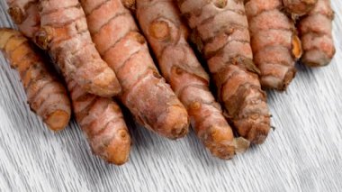 Beyaz ahşap bir dokuda birçok organik kökleri var. Tamamen çiğ zerdeçal rizom. Hint doğal baharatı. Sağlıklı malzemeler. Yiyeceklerdeki antioksidanların kaynağı