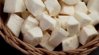 Ahşap bir masanın üzerinde doğranmış manyok (yucca) dilimlenmiş kök ve rustik rattan kasesi. Döndürme