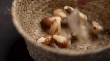 Kurumuş organik Brezilya fındıkları, koyu kahverengi ahşap arka planda ağır çekimde kırsal bir hasır kaseye düşüyor..