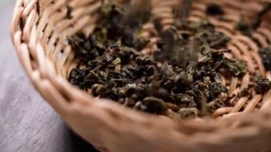 Barut yeşili, kurutulmuş çay yaprakları ahşap masadaki ahşap bir rattan kaseye dökülüyor. Çin geleneksel aromatik içecek malzemesi. Ağır çekim. Döndürme