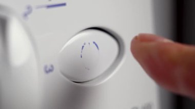Beyaz çamaşır makinesindeki kırmızı düğmeye basan bir parmağın yakın plan görüntüsü. Cihazı kapatıyor.