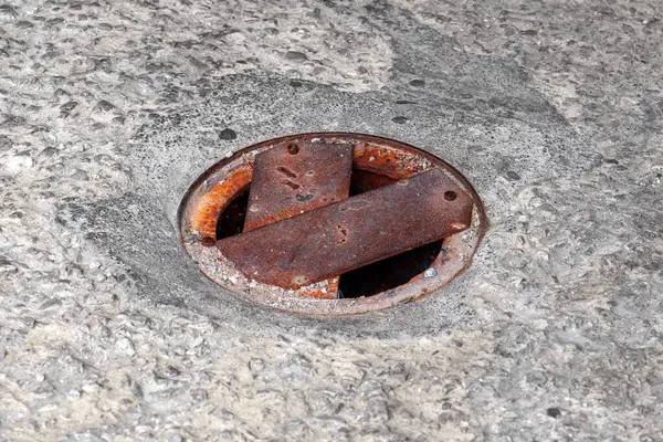 Beton bir yolda yuvarlak drenaj kuyusu elle metal levhalarla kaplıdır ve yıpranmış bir görünüşü vardır.