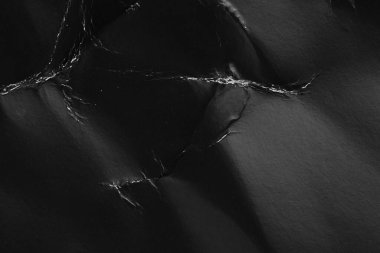 Kırışmış kağıt dokuları ve kırışıklıkları olan siyah monokrom görüntü. Soyut tasarım, karton paketlerin doğal kıvrımlarını ve kıvrımlarını vurgular.