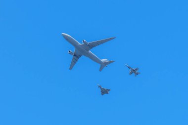 Gijon, İspanya - 24 Mayıs 2024: Büyük bir kargo uçağı, yanında iki küçük avcı uçağı ile gökyüzünde uçuyor. Açık mavi gökyüzünde uçağın siluetleri beliriyor